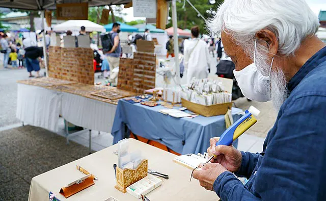 平安楽市：平安楽市の名物出店者であるレザーバーニングアートの「SAKANA（サカナ）」さん。購入した作品には、その場で名前を焼き付けてもらえます