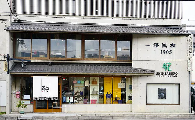 一澤信三郎帆布：帆布製のかばん専門店なので、暖簾や外壁には布に包むと書いて“かばん”という文字が記されています。「京都で作って、京都で売る」というモットーのもと、お店のすぐそばに工房があり、一部外から見学できます