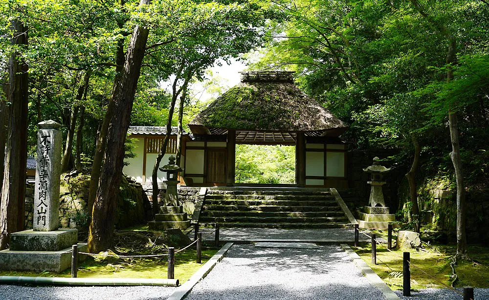 法然院：瑞々しい緑に包まれた茅葺きの山門。門前の石碑には「不許葷辛酒肉入山門」の文字が刻まれています